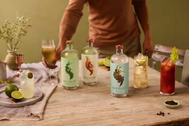 A table with several three bottles of Seedlip's different Non-Alcoholic Spirits and four different glasses filled with the beverages.
