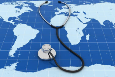 A map of the world in all blue with a stethoscope laying on top of it.