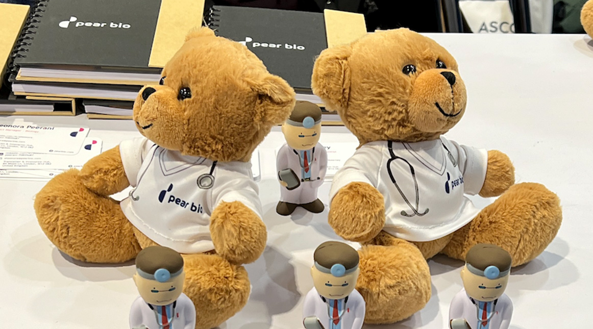 A table from the Pear Bio booth at ASCO 2023 with two stuffed beards wearing a shirt that says Pear Bio and also has an image of a stethoscope. There are also smaller doctor figurines. 