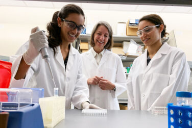 Kathryn Kundrod, Rebecca Richards-Kortum, and Mary Natoli working in Richards-Kortum’s Rice University laboratory. Kundrod is filling up a vial while the other two watch standing nearby.