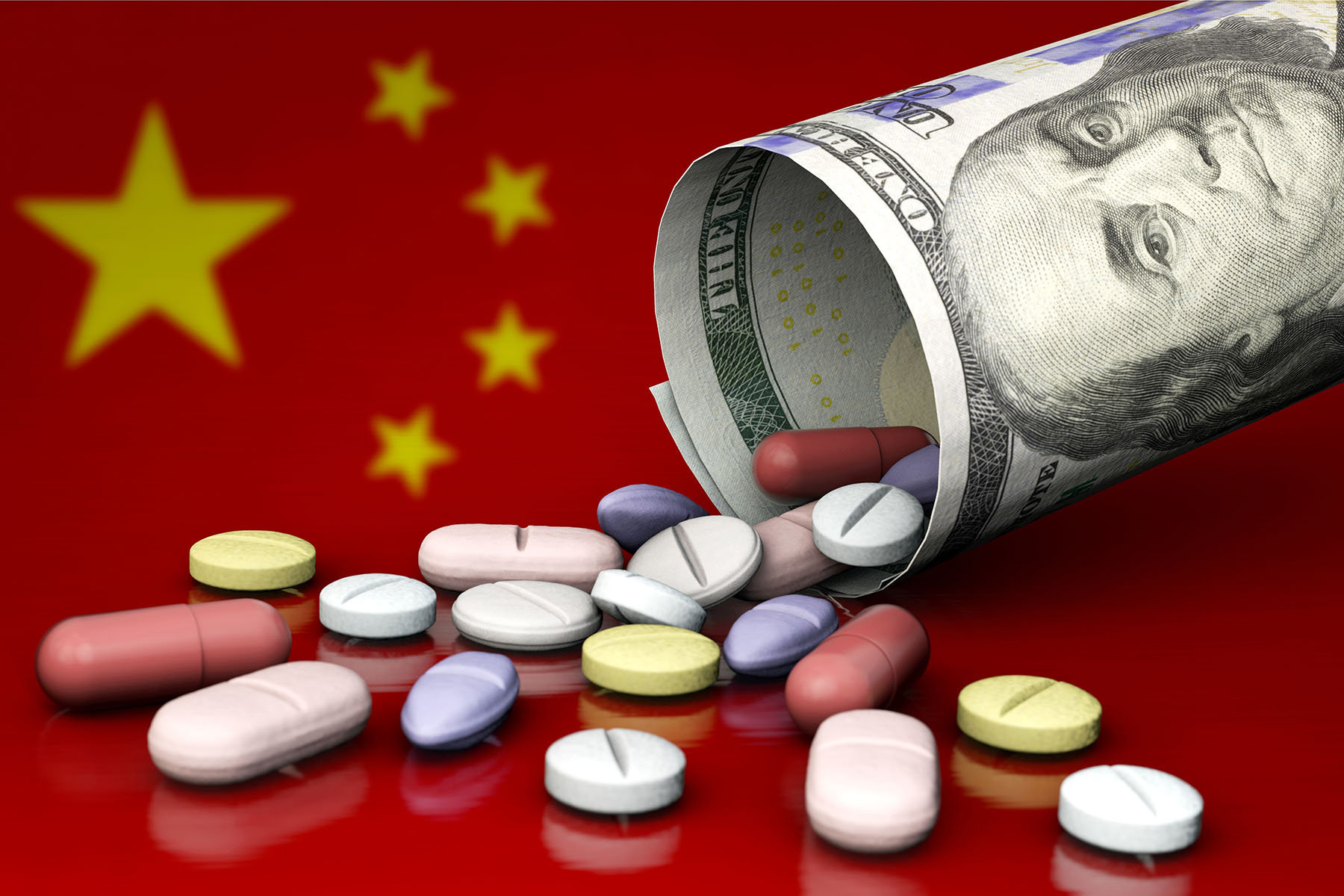 A rolled up $100 U.S. bill dumping various medical pills onto the Chinese flag